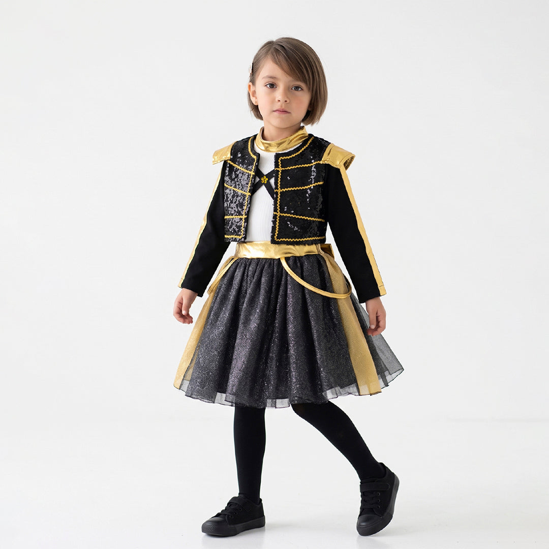 Niña de cuerpo entero con atuendo negro de detalles dorados, chaqueta corta y falda amplia, sobre un fondo blanco.