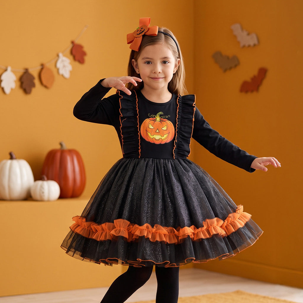 Niña con vestido negro de Halloween, calabaza al frente y olanes naranjas en la falda, sobre un fondo con decoración otoñal.