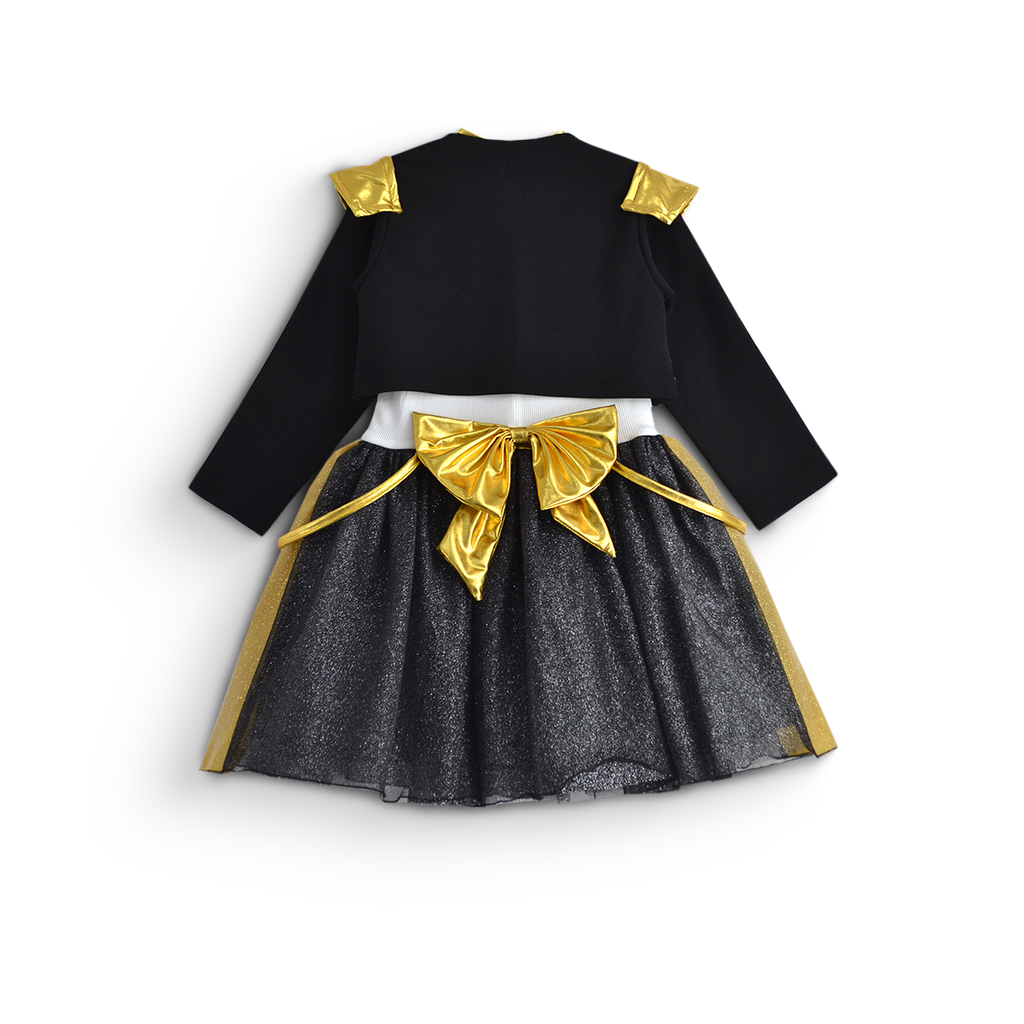Vista trasera de conjunto infantil con chaqueta negra de manga larga, detalles dorados y falda negra brillante con moño dorado.