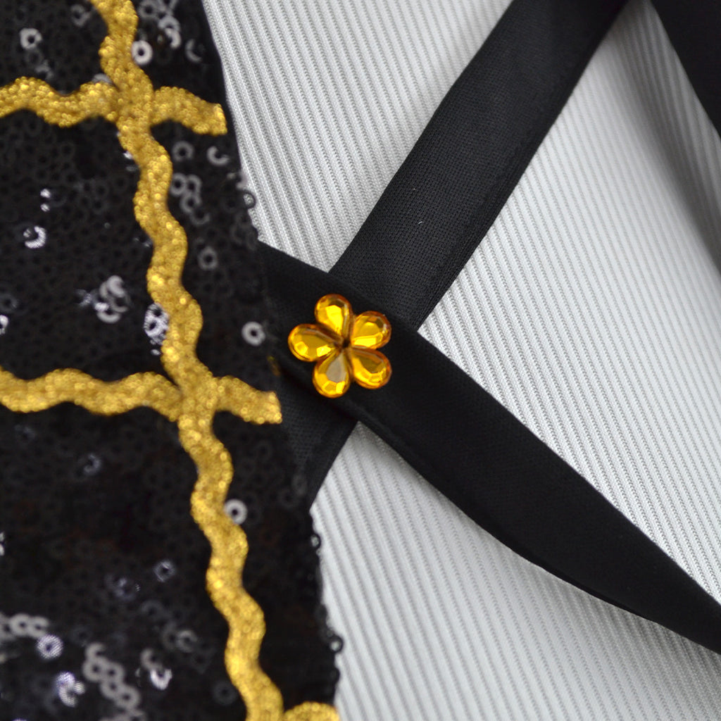 Detalle de las tiras negras cruzadas con adorno de flor dorada y ribete dorado en la chaqueta.