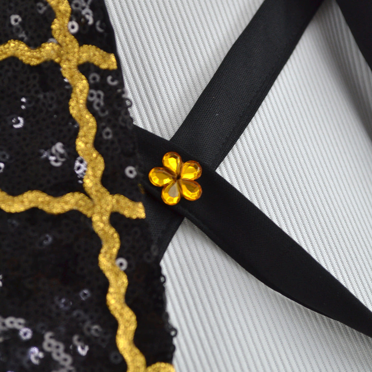 Detalle de las tiras negras cruzadas con adorno de flor dorada y ribete dorado en la chaqueta.