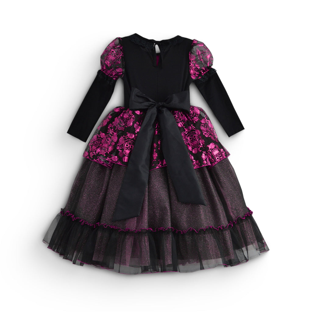 Vista trasera de vestido infantil negro de manga larga, con estampado fucsia de calaveras y flores, lazo en la cintura y falda de tul en capas.