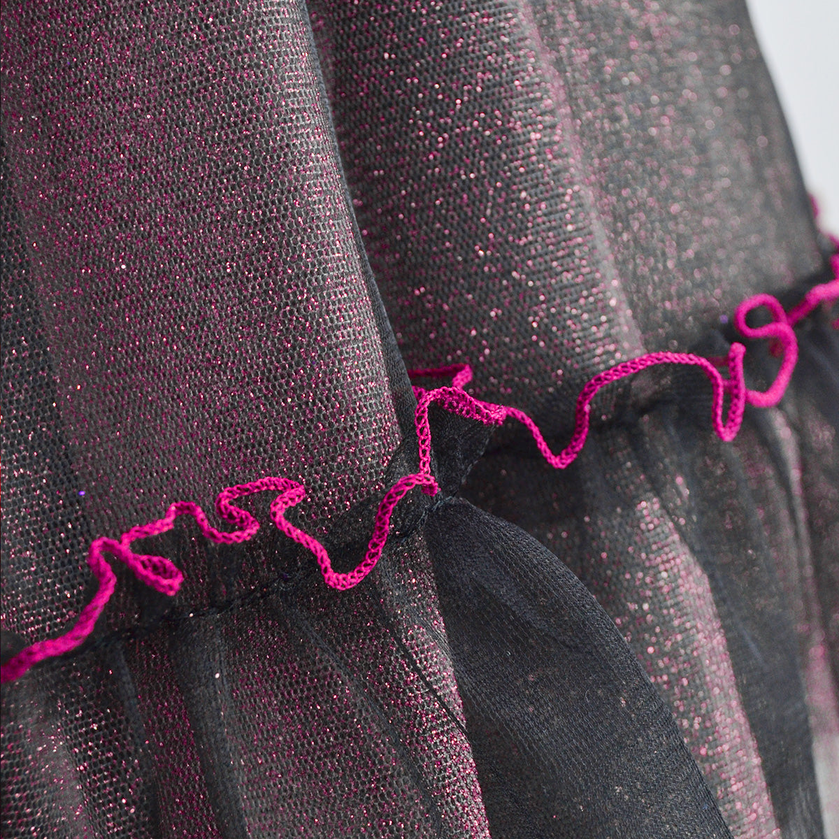 Detalle de la falda de tul negro brillante con ribete ondulado color fucsia.