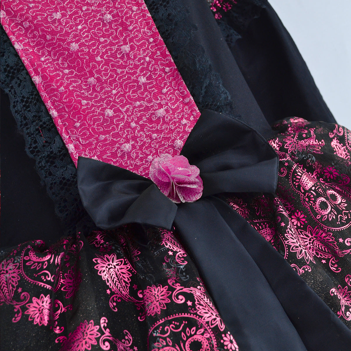 Detalle del vestido negro con panel fucsia, moño negro y flor rosa en la cintura, sobre tela estampada con calaveras y flores.