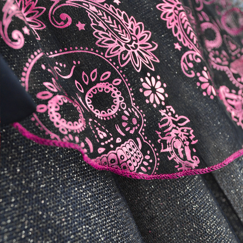 Detalle de tela negra con estampado rosa de calaveras y flores, ribete fucsia y acabado brillante.