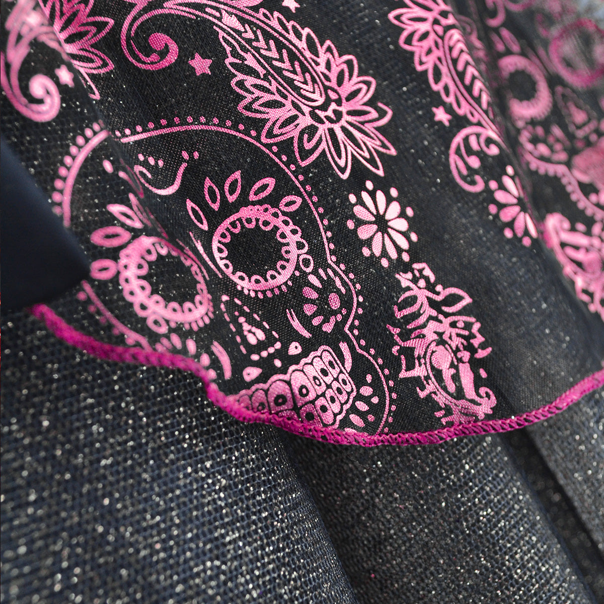 Detalle de tela negra con estampado rosa de calaveras y flores, ribete fucsia y acabado brillante.