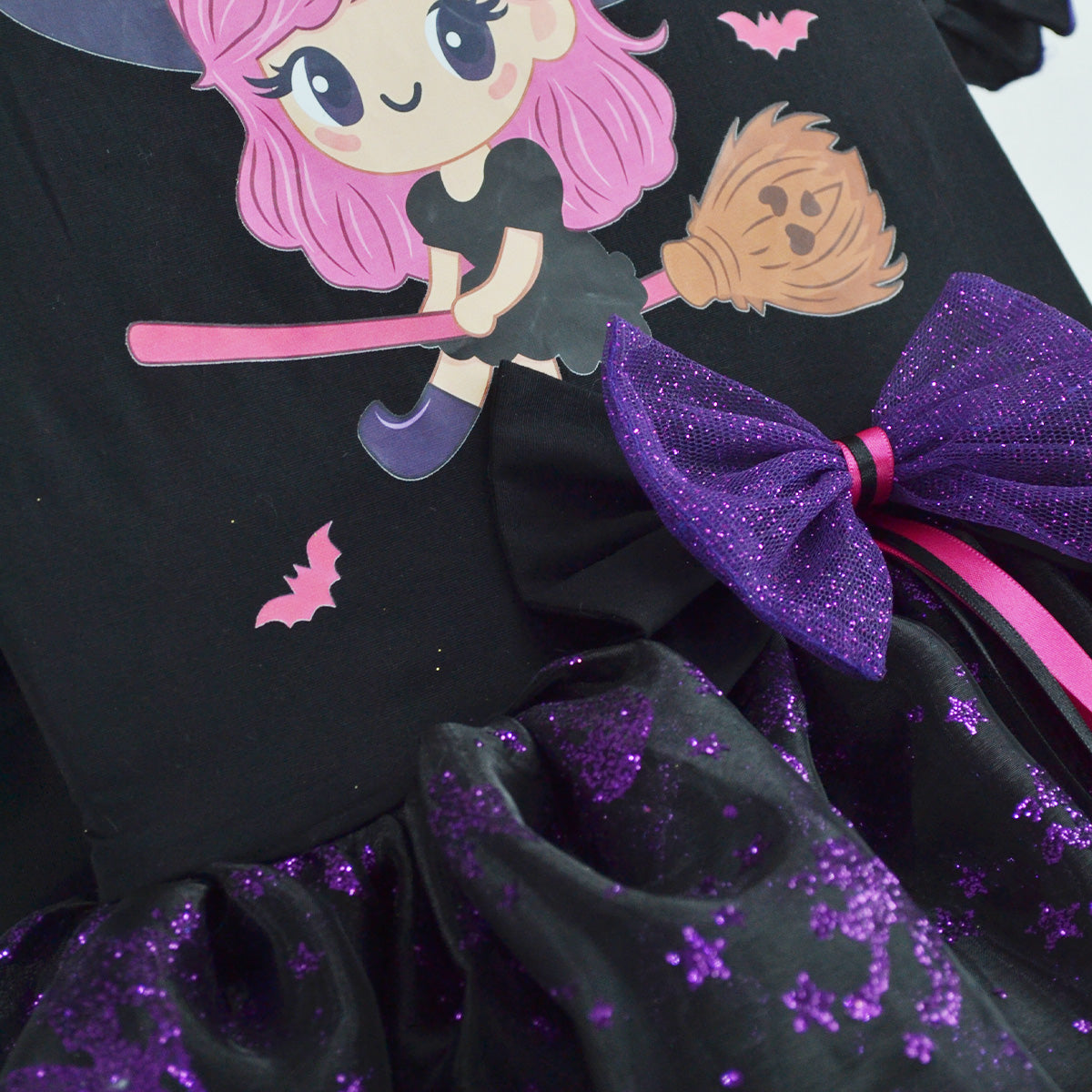 Detalle de vestido negro de brujita con ilustración, moño morado brillante y falda con destellos morados.