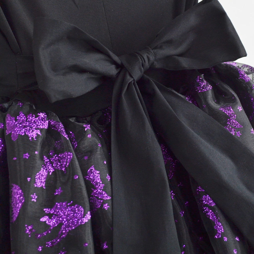 Detalle del vestido negro con lazo en la cintura y estampado morado brillante.